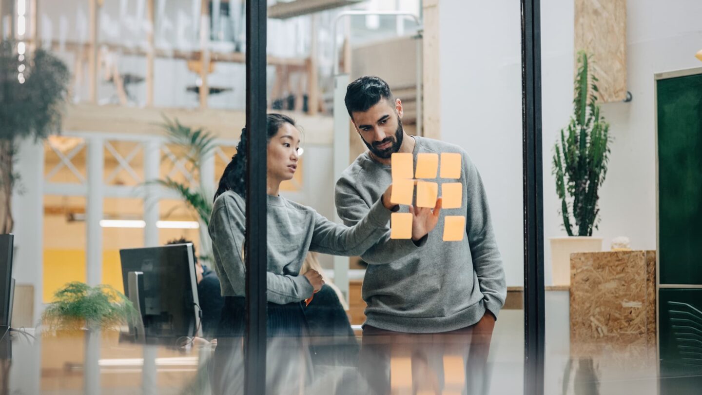 Dois colegas de trabalho em frente a uma apresentação com post-its, colaborando e discutindo ideias