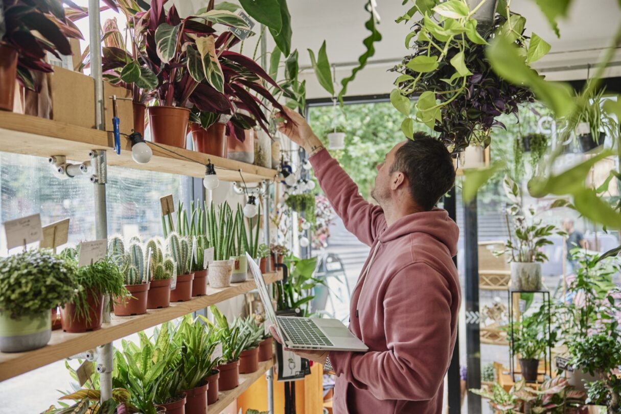 Empreendedor sorridente no seu negócio de plantas, rodeado por uma variedade de plantas verdes.