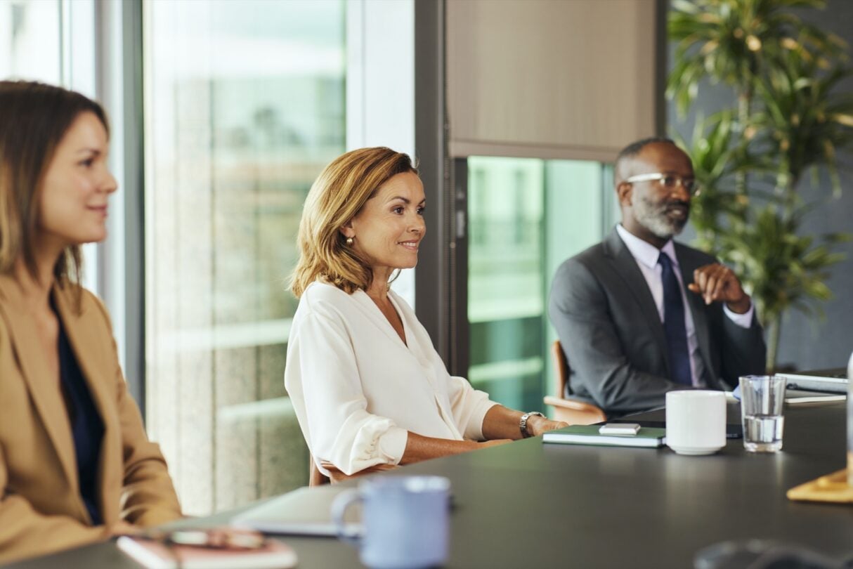 Mulher jovem sentada à mesa durante uma reunião de trabalho, com expressão atenta e postura profissional